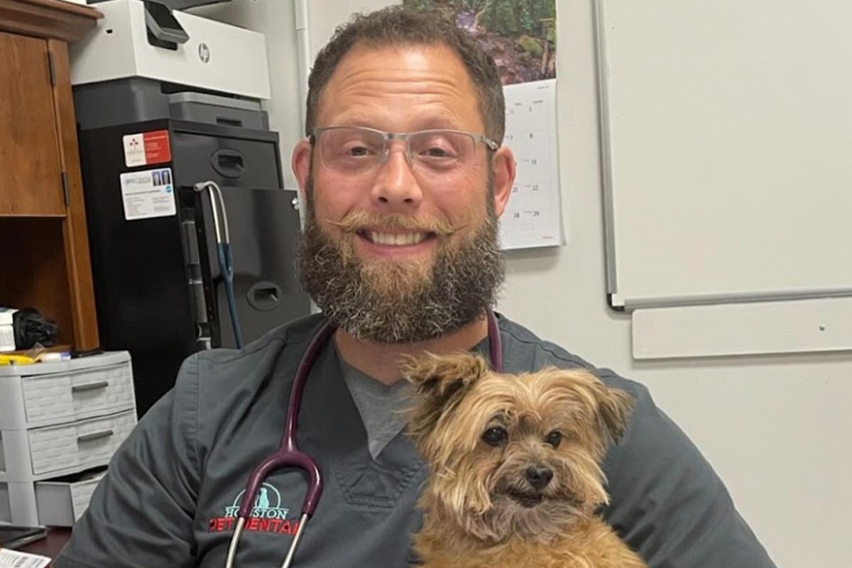 male veterinarian smiling and holding fluffy small dog